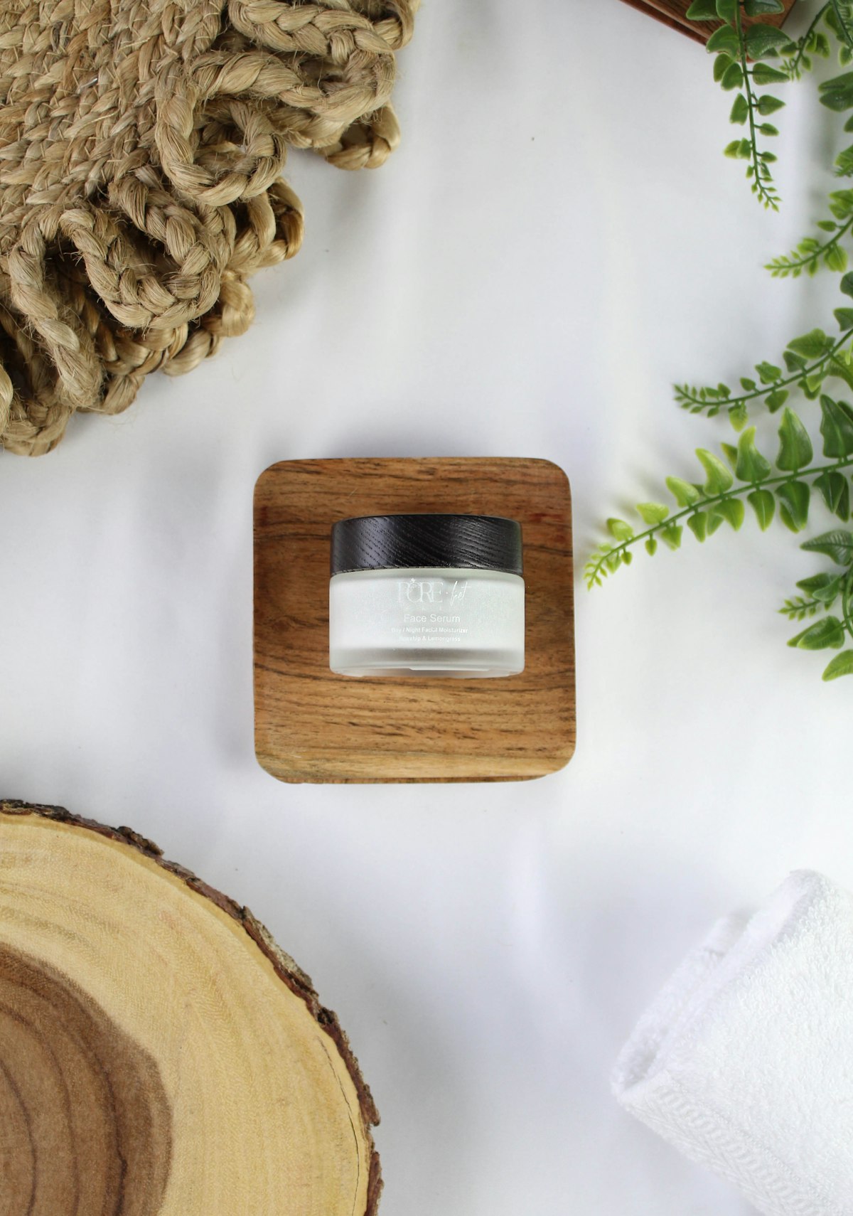 A small glass cream jar on a wooden stand surrounded by ferns