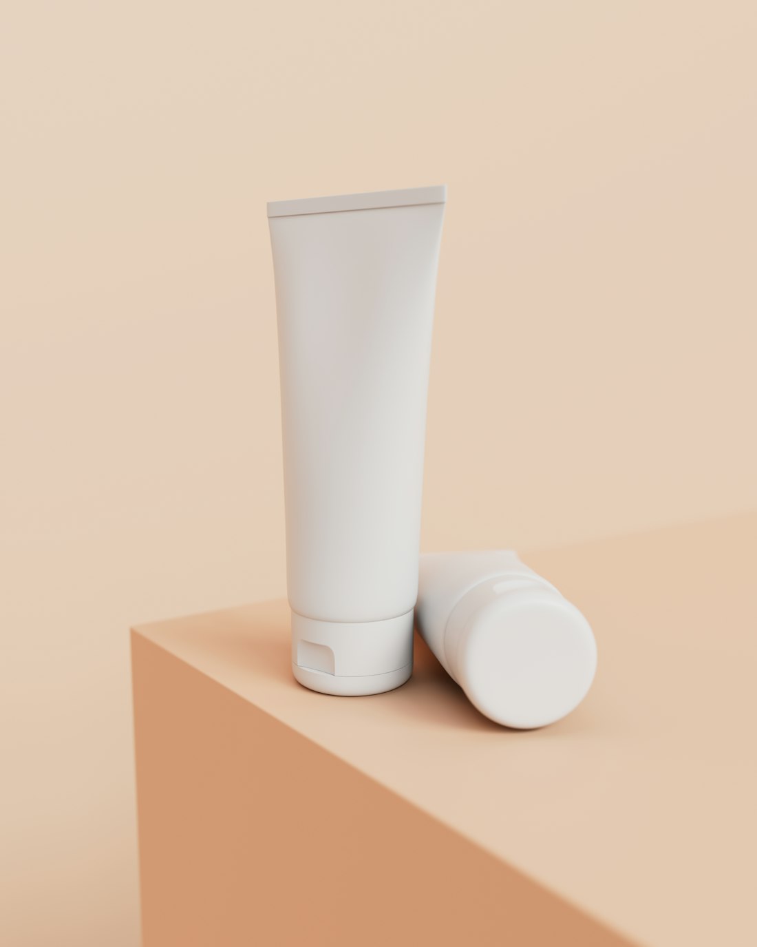 A white squeeze tube and a round bottle on a soft peach surface