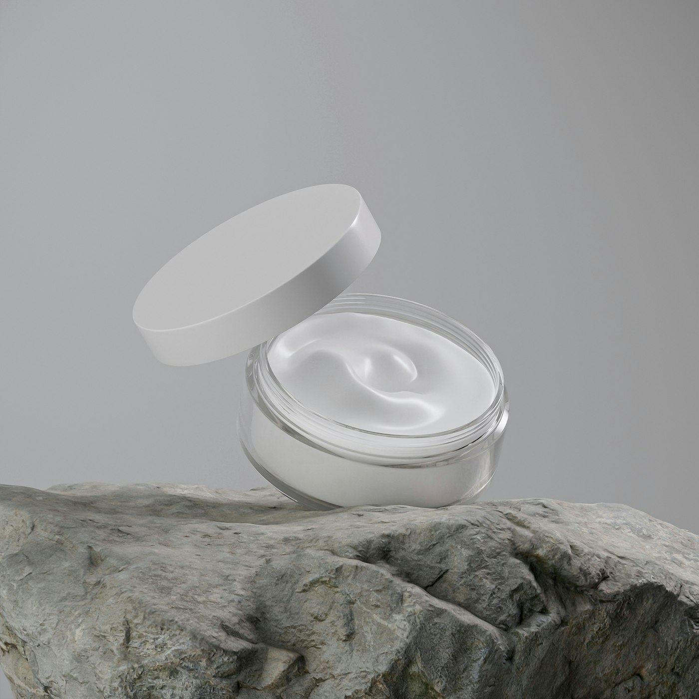 An open white cosmetic jar of cream resting on a grey stone